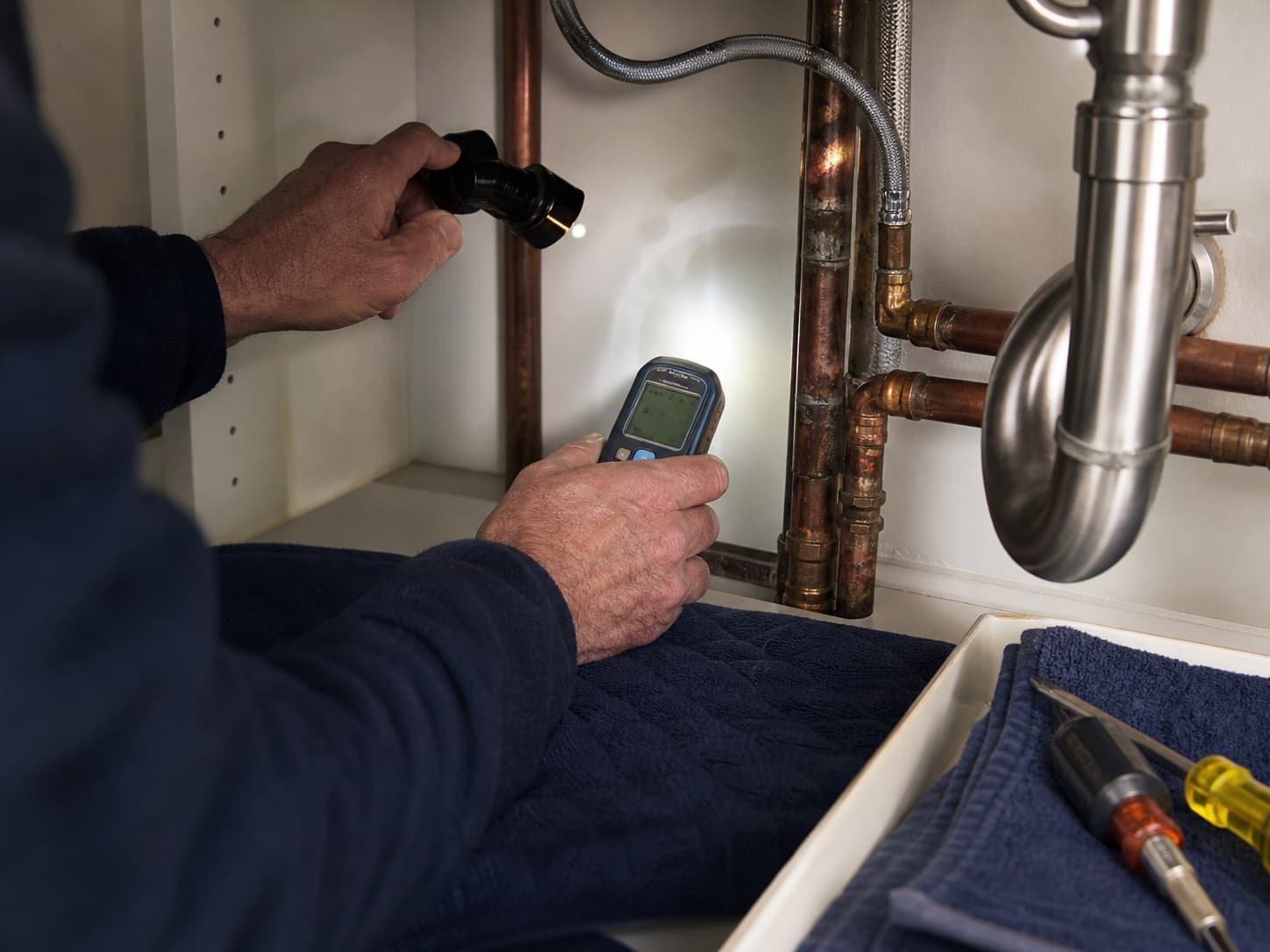 A licensed plumber uses a moisture meter and inspection light to diagnose a leak